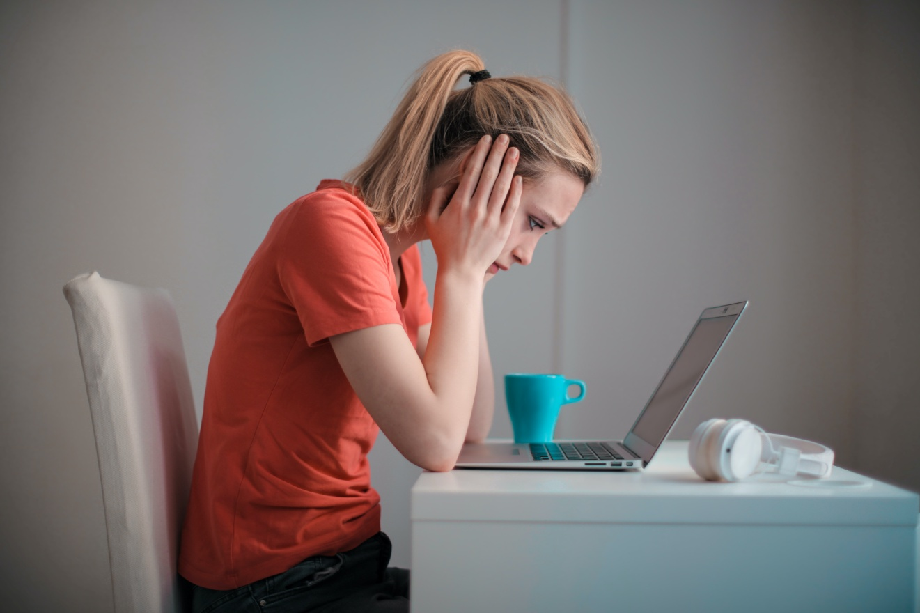 A woman looking at her laptop with her face in her hands